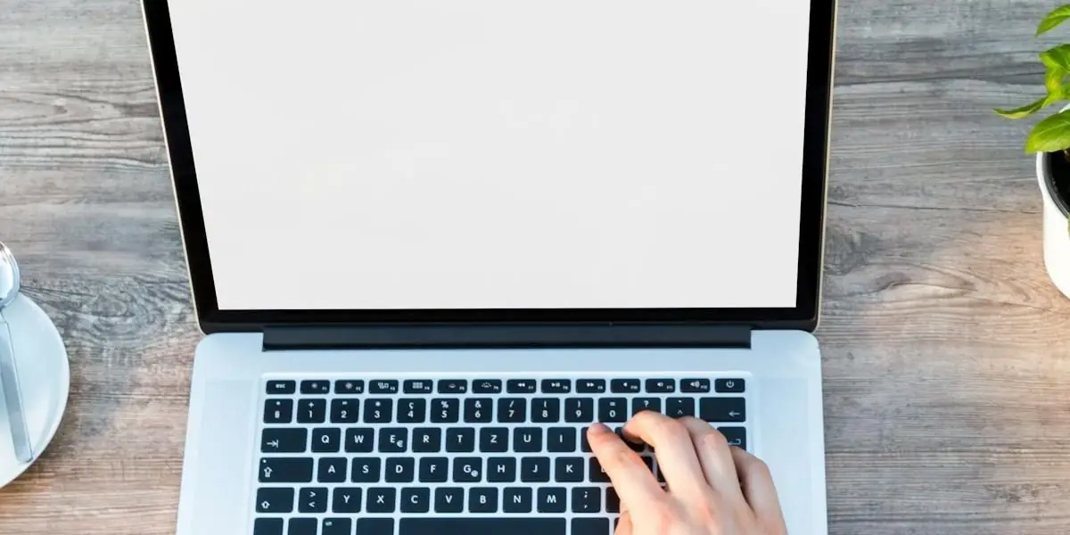 Hände tippen auf einem aufgeklappten Laptop, der auf einem Holztisch steht